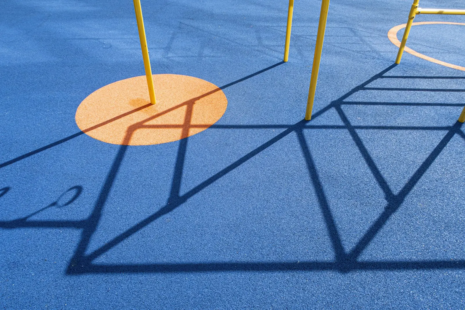 Blue rubber safety surface with an orange circle inset under play equipment