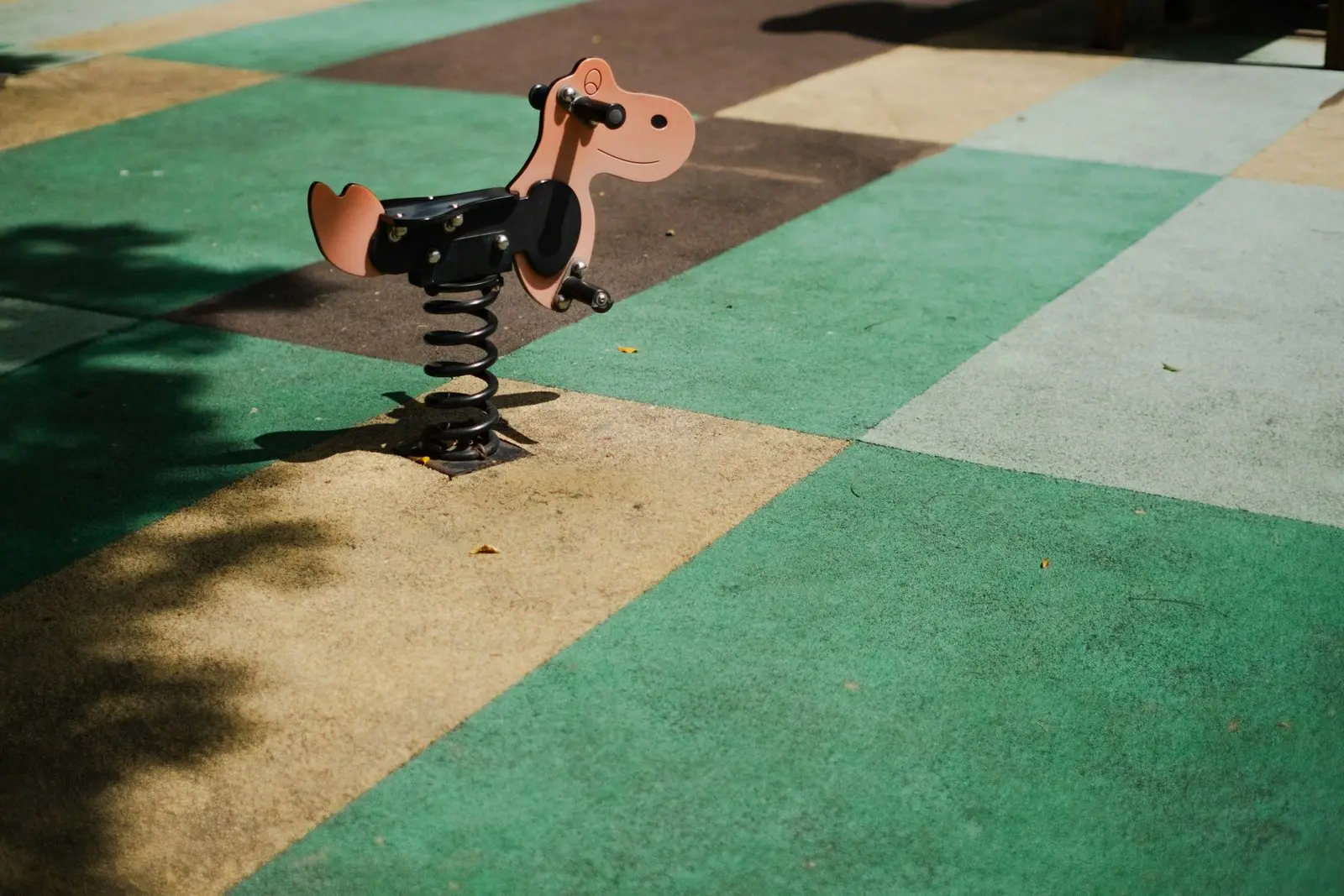 Spring rider on a playground with green and beige safety surfacing